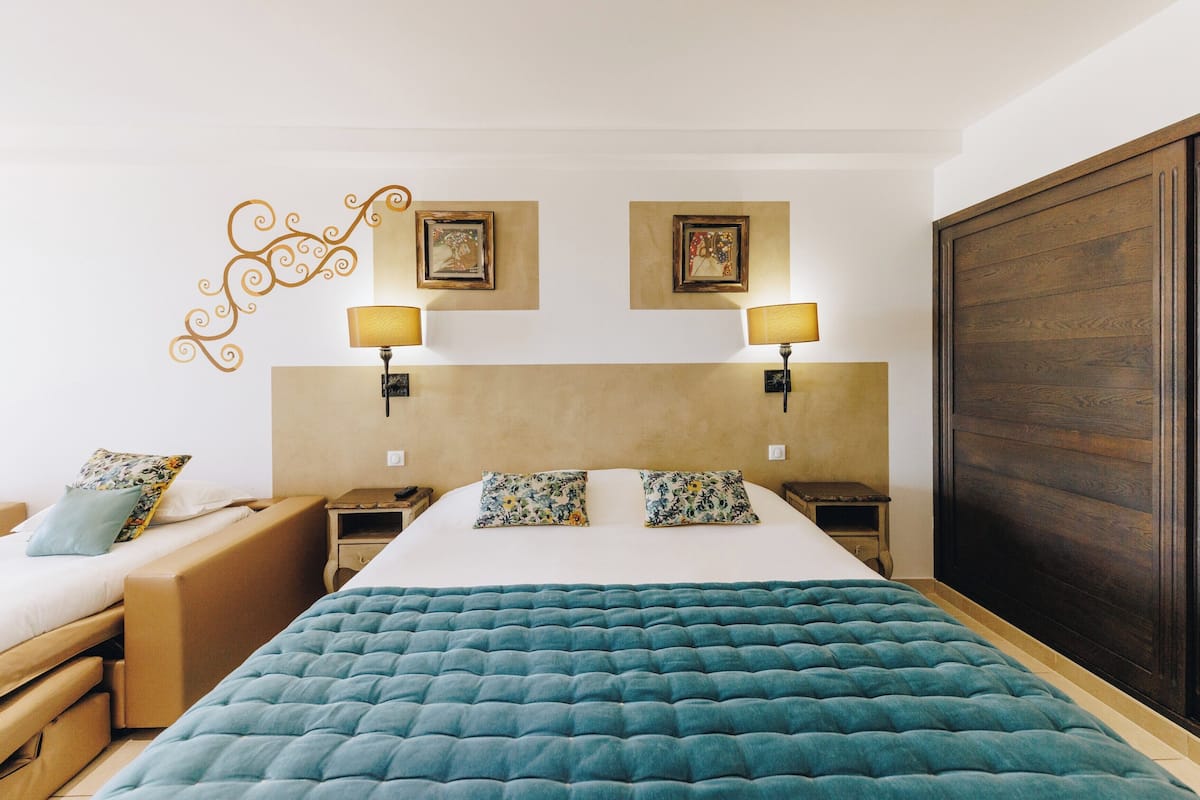A hotel room with a large bed, two bedside tables, a nightstand, a sofa, and a wardrobe.