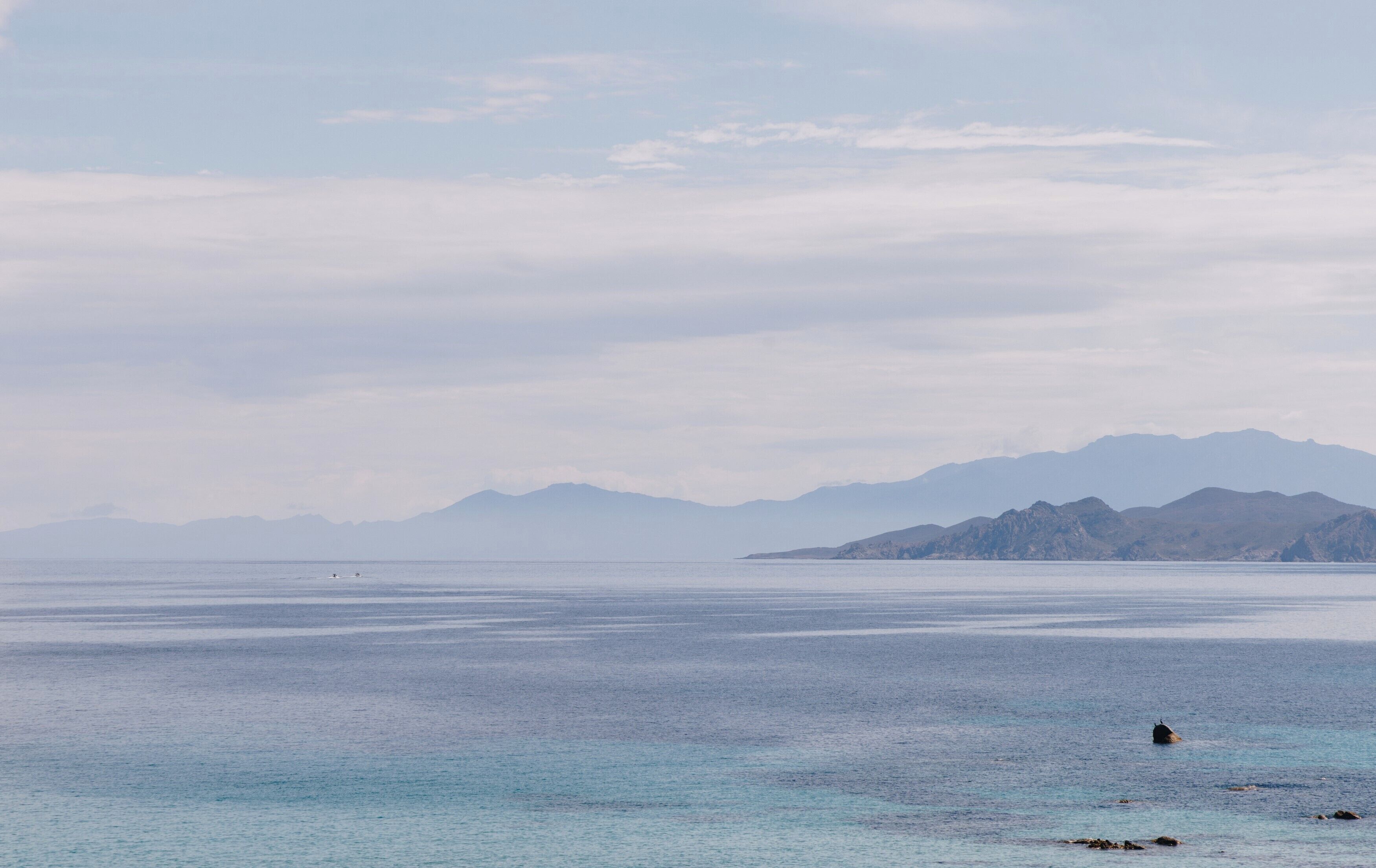 Un mar tranquilo con montañas lejanas y cielo despejado.