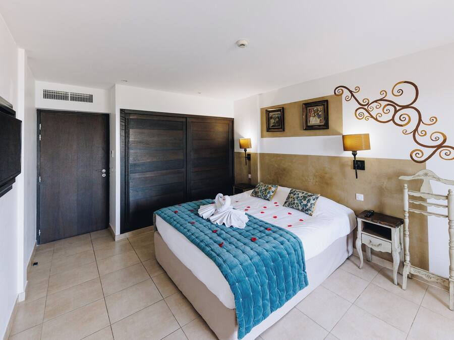 A hotel room with a bed, a wardrobe, a TV, a lamp, and a decorative wall piece.