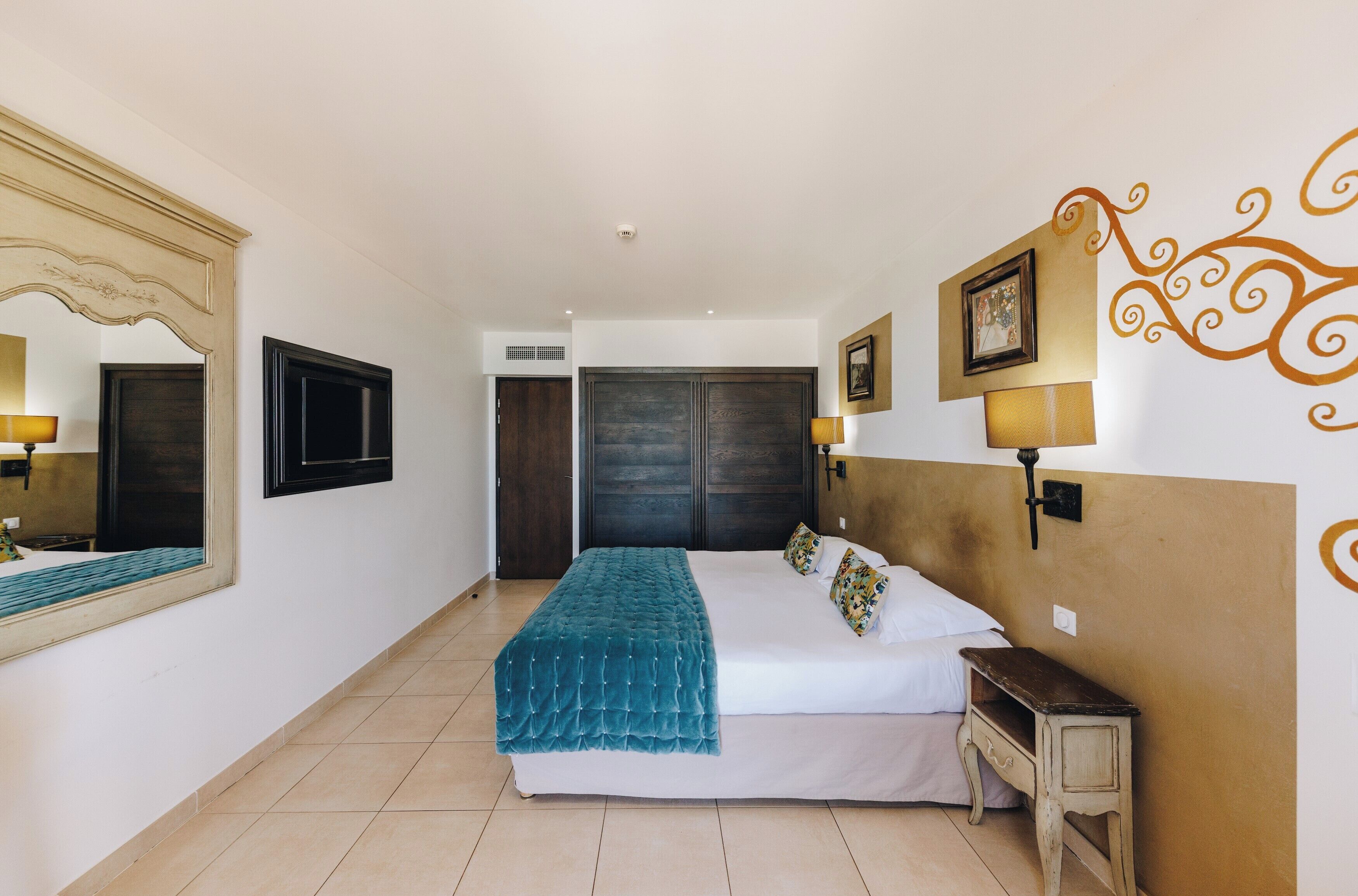 A bedroom with a bed, bedside table, wall-mounted lamp, and a large mirror.