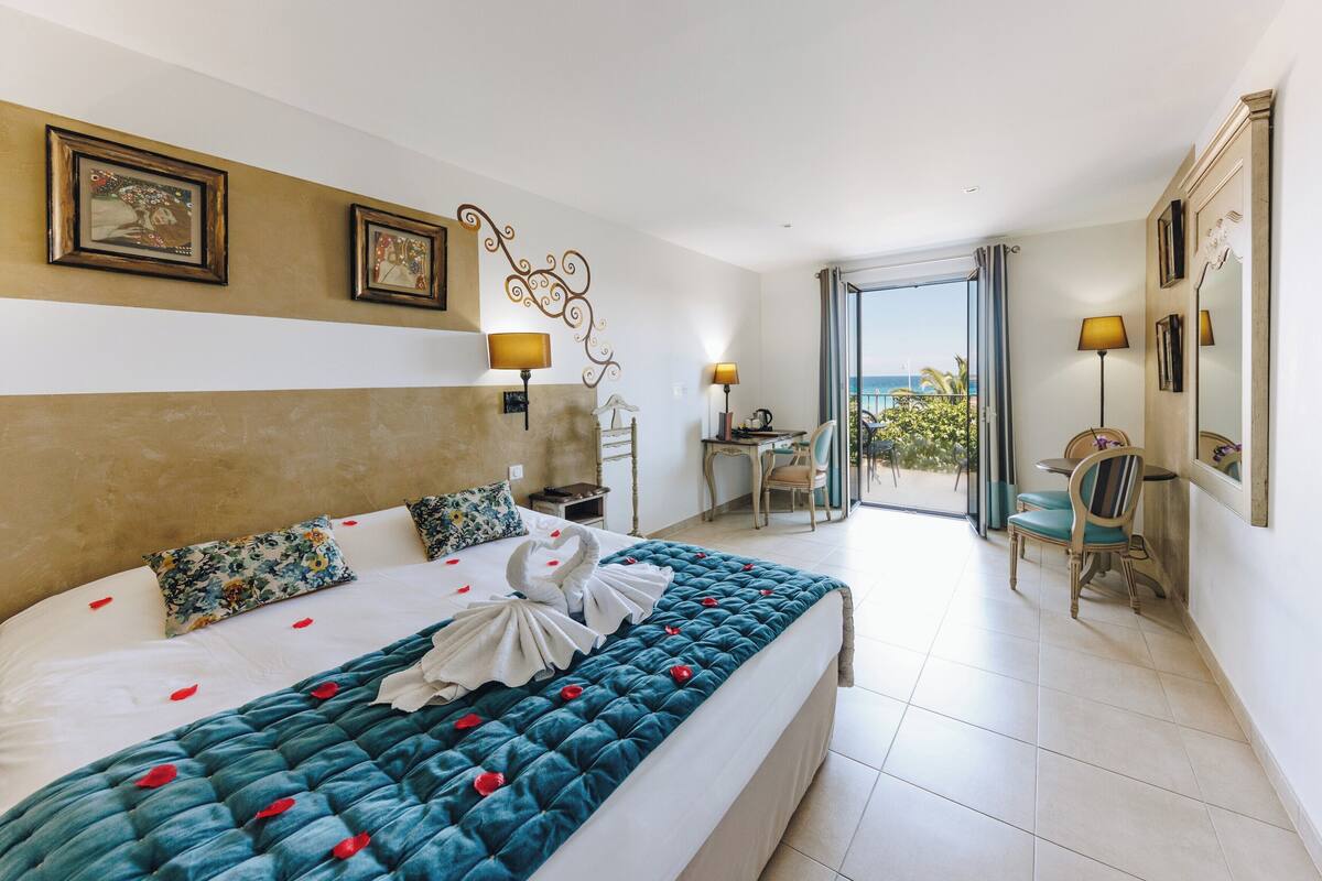 A hotel room with a large bed, a balcony with a view, and a dining area.