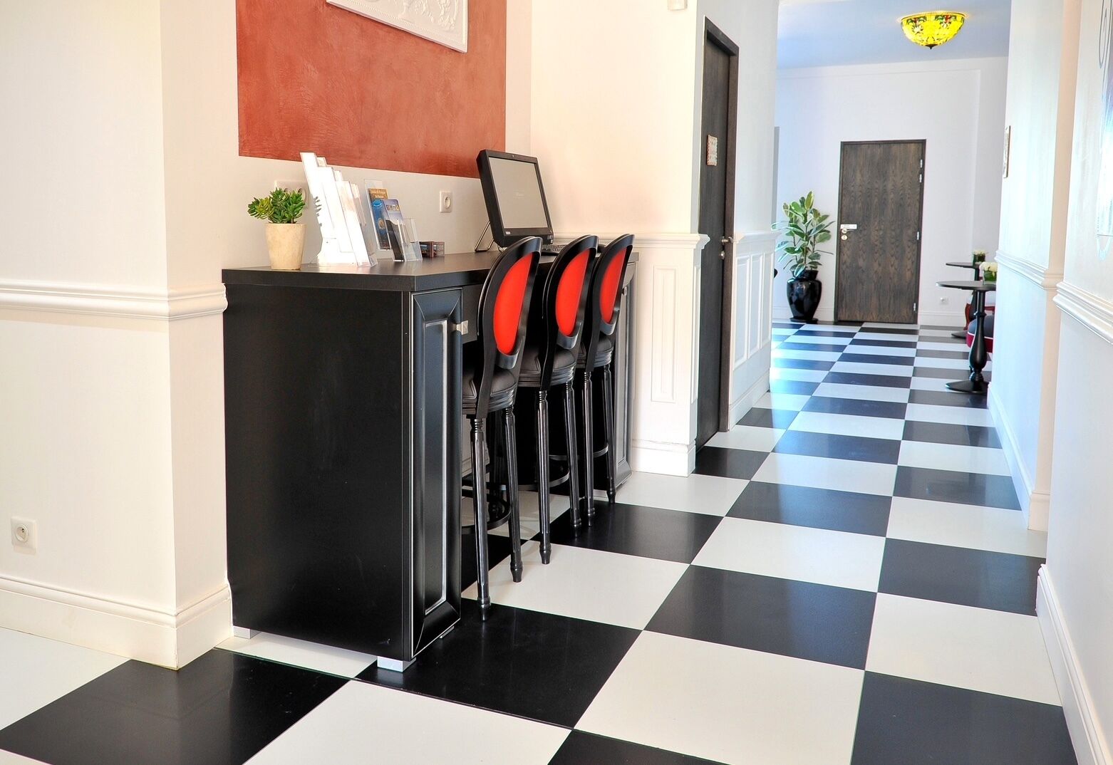 Un hall d’hôtel avec un sol à carreaux, un comptoir d’accueil et des chaises rouges.