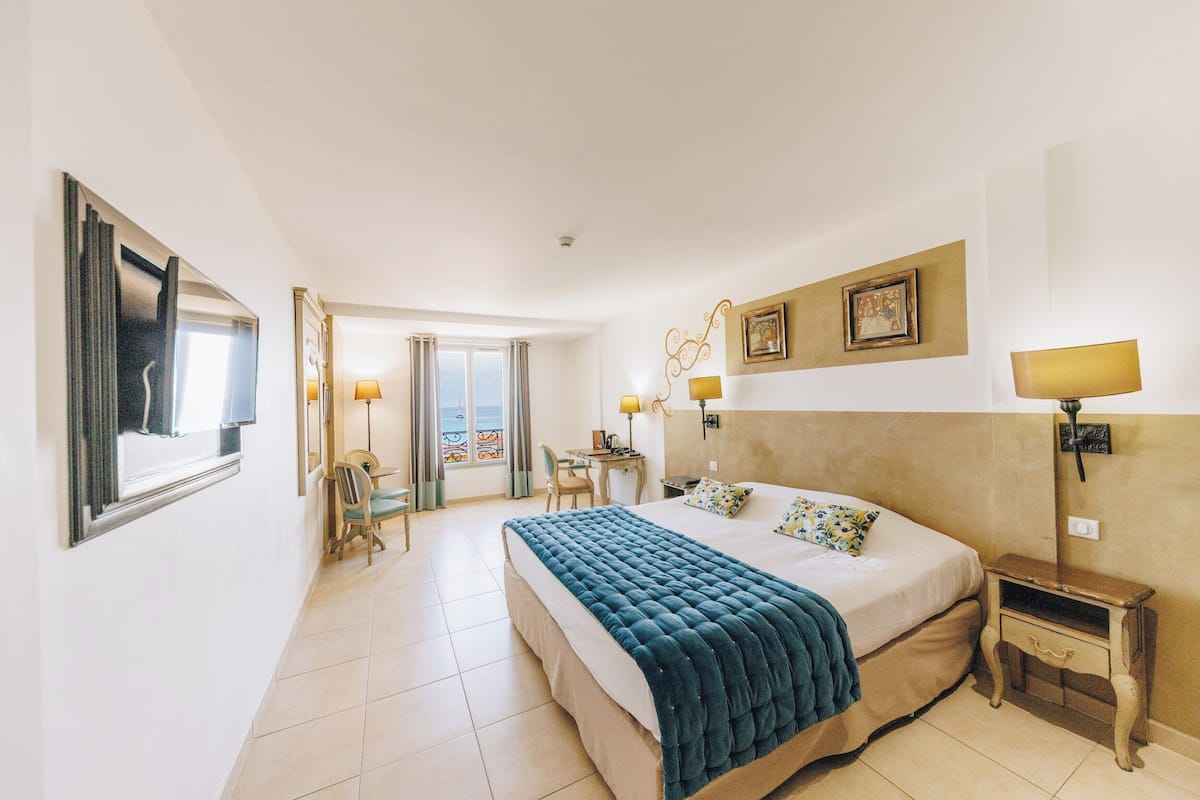 A hotel room with a large bed, a desk, a chair, and a view of the sea through a window.