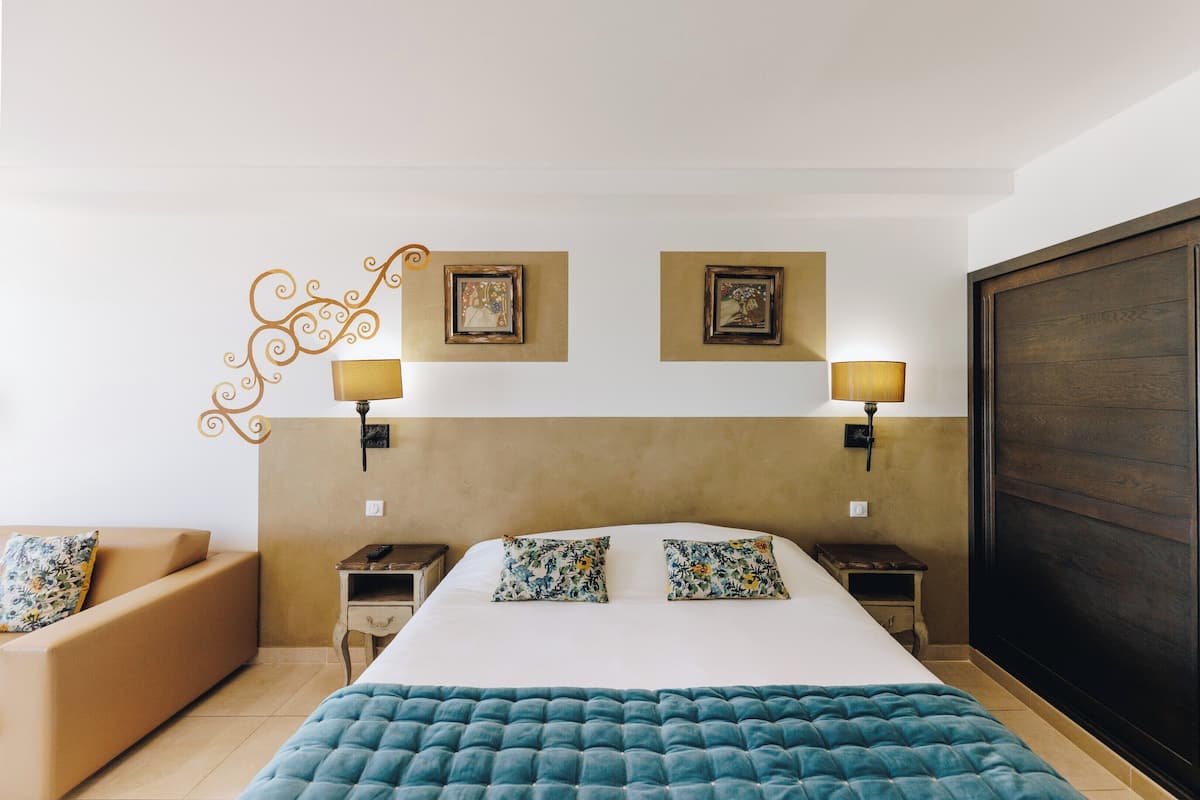 A hotel room with a large bed, two bedside tables with lamps, a sofa, and a wardrobe.