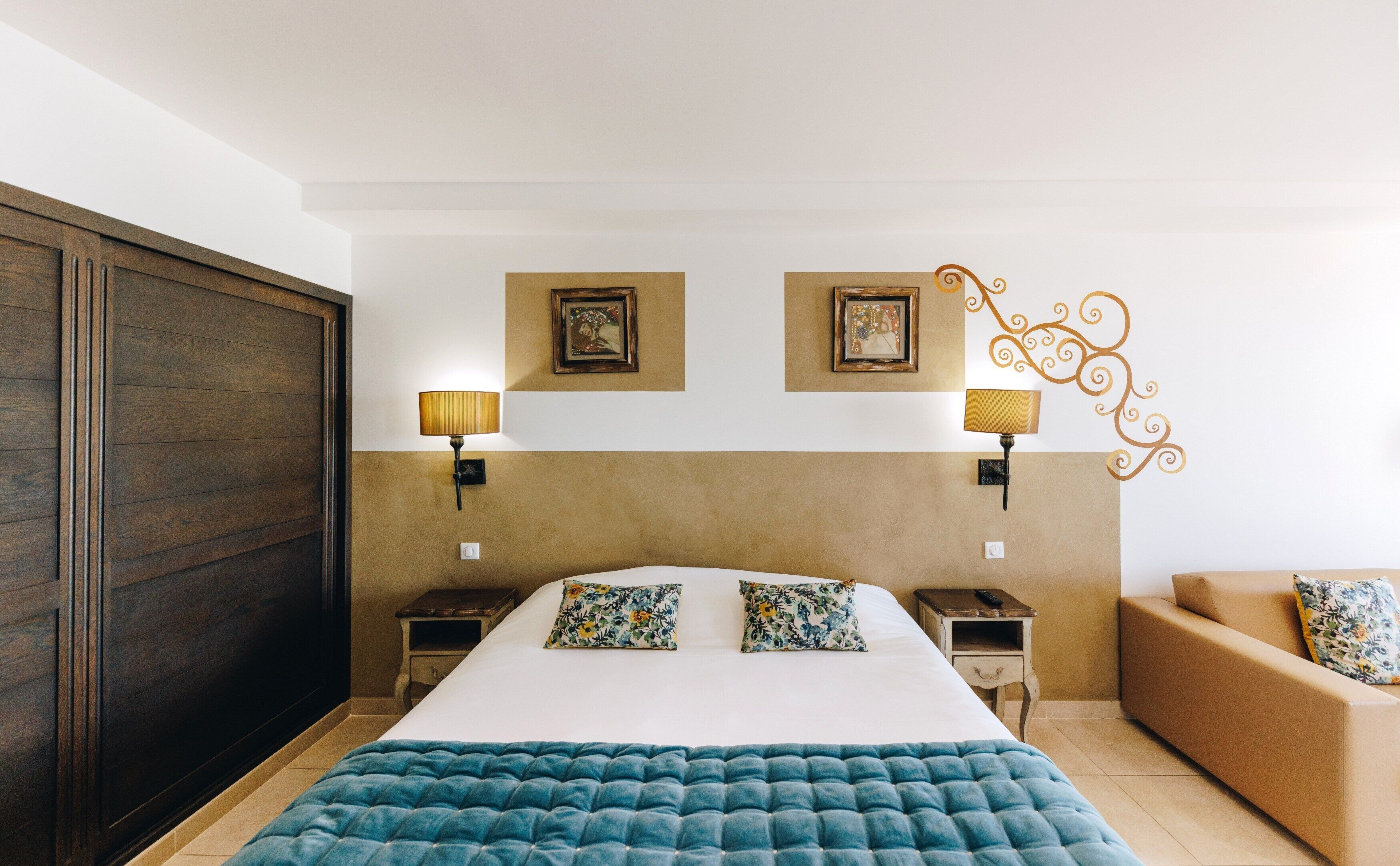 Un dormitorio con una cama grande, dos mesitas de noche, un pequeño sofá y lámparas fijadas a la pared.