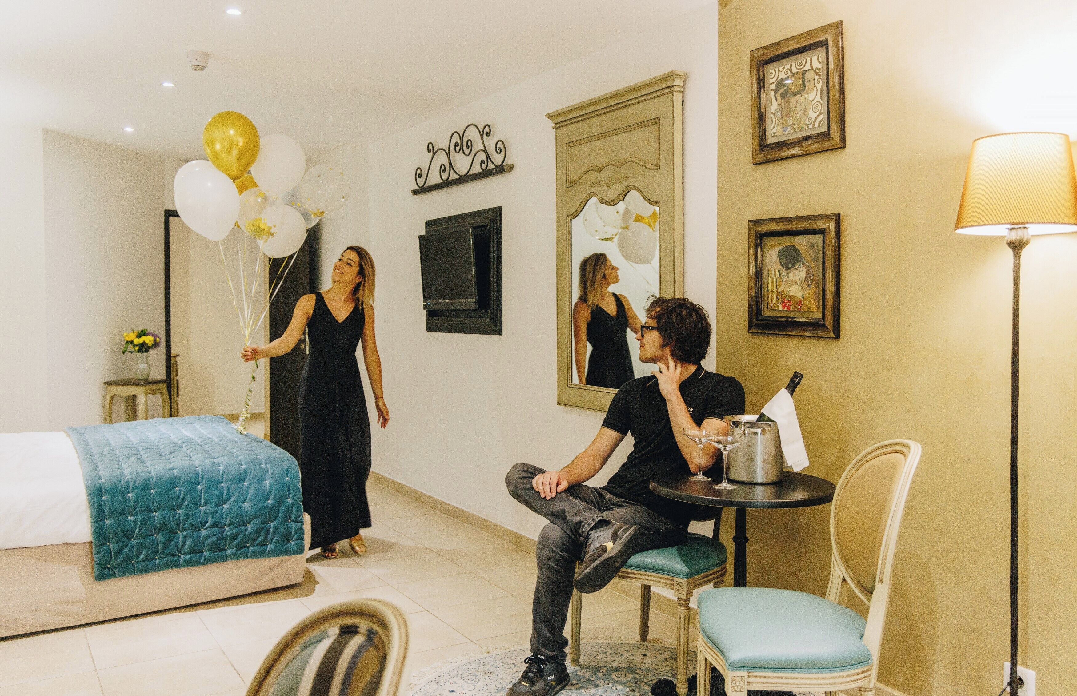 A hotel room with a bed, a dining table with chairs, a lamp, and a wall with framed artwork.