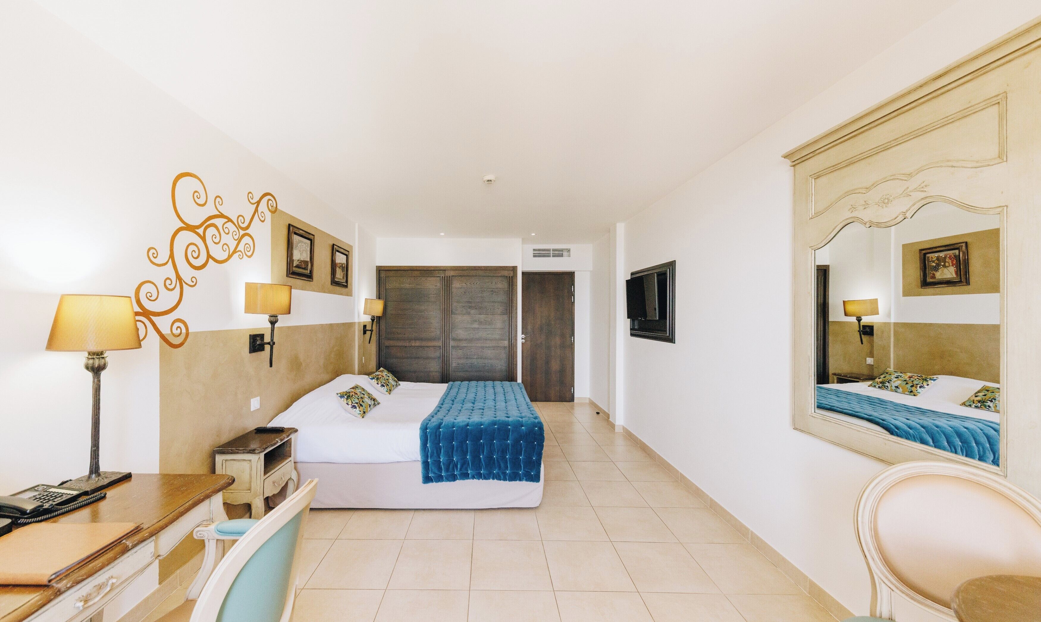 A hotel room with a bed, bedside lamps, a desk with a telephone, a chair, and a large mirror.