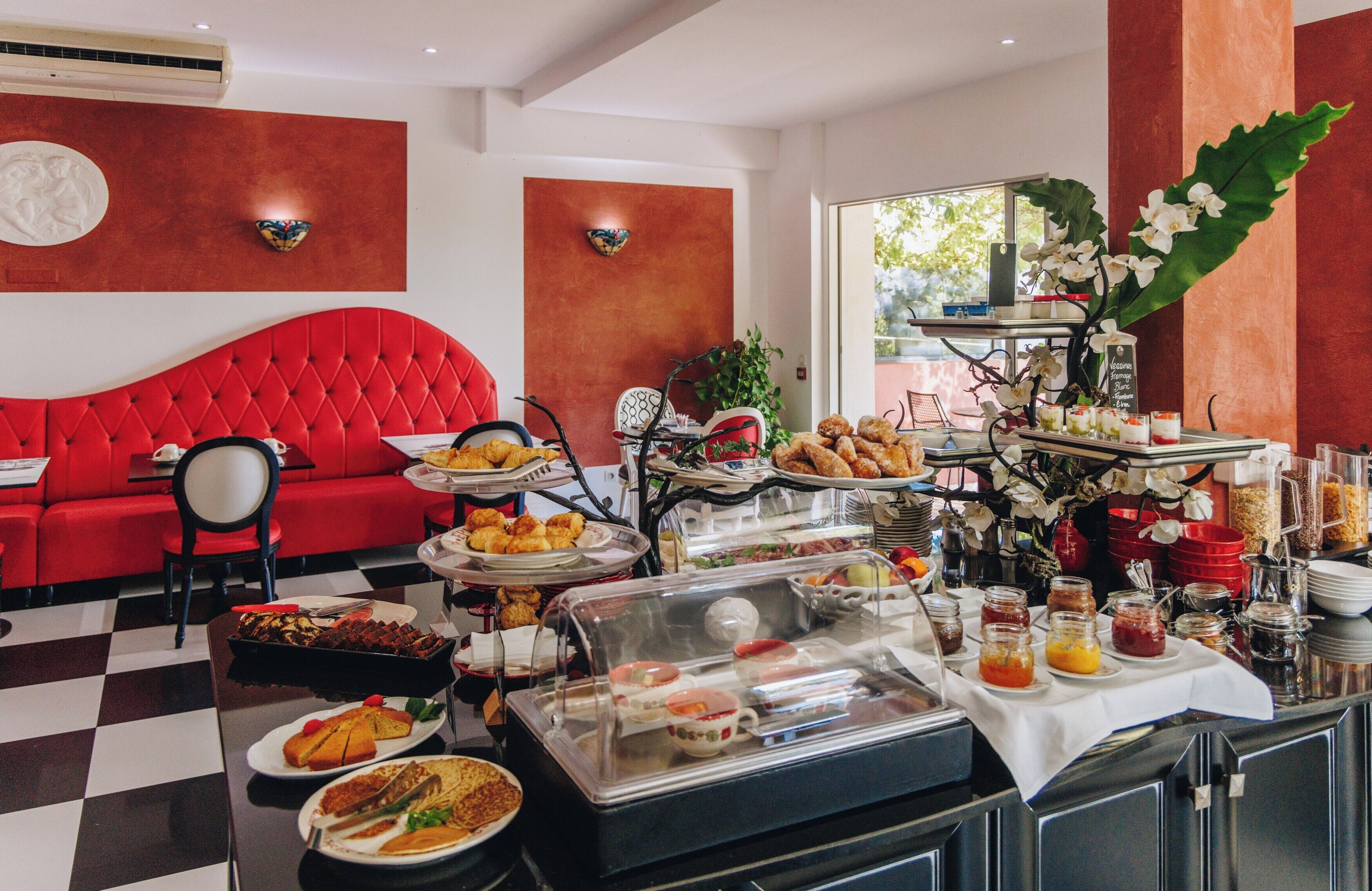 Um buffet de café da manhã com diversos alimentos e um sofá vermelho ao fundo.