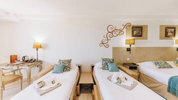 Habitación de hotel con dos camas individuales, un escritorio con lámpara, una silla y una mesita con hervidor.
