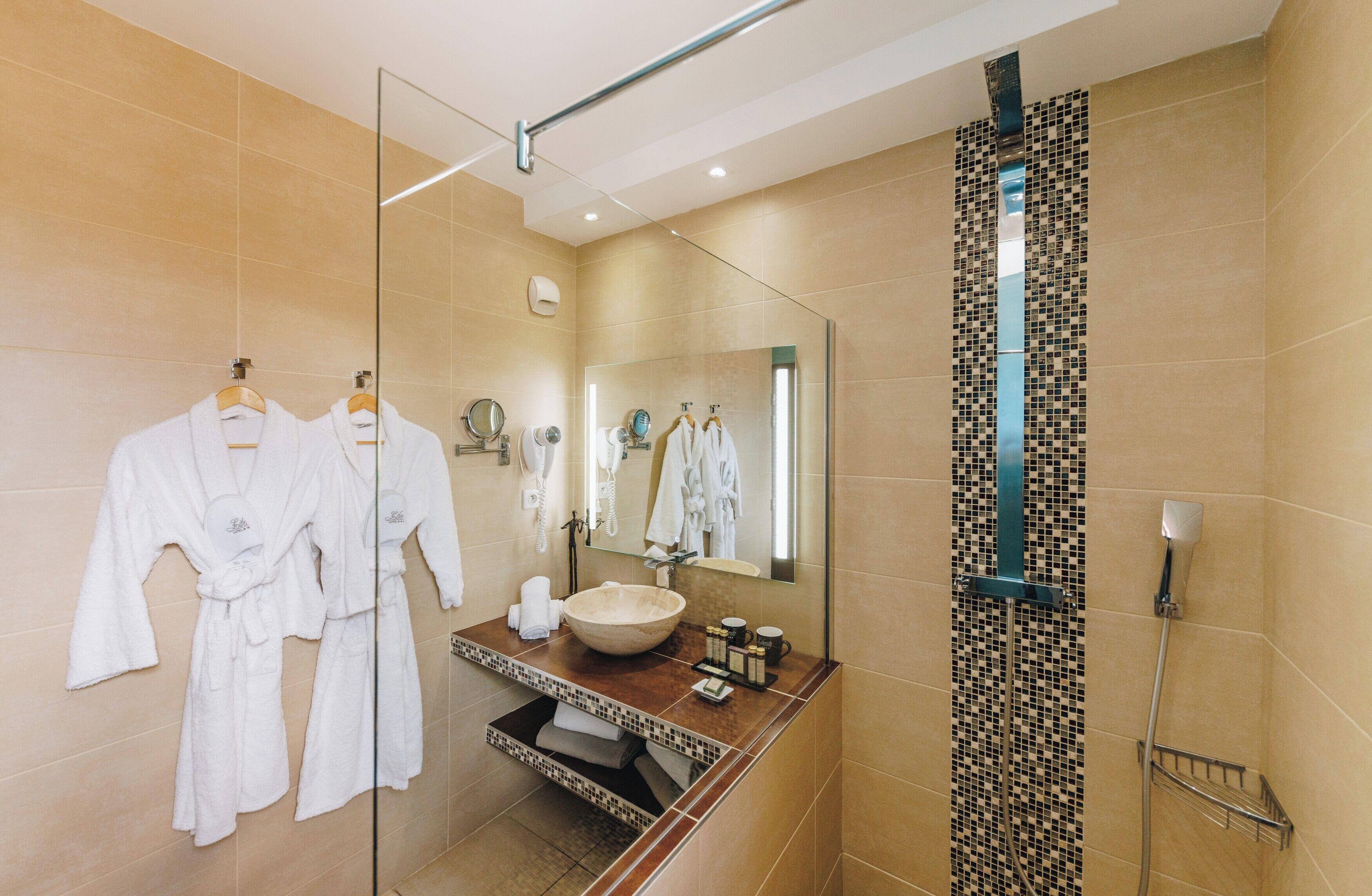 A modern bathroom with a large mirror, a sink with a vessel basin, and two white robes hanging on a rack.