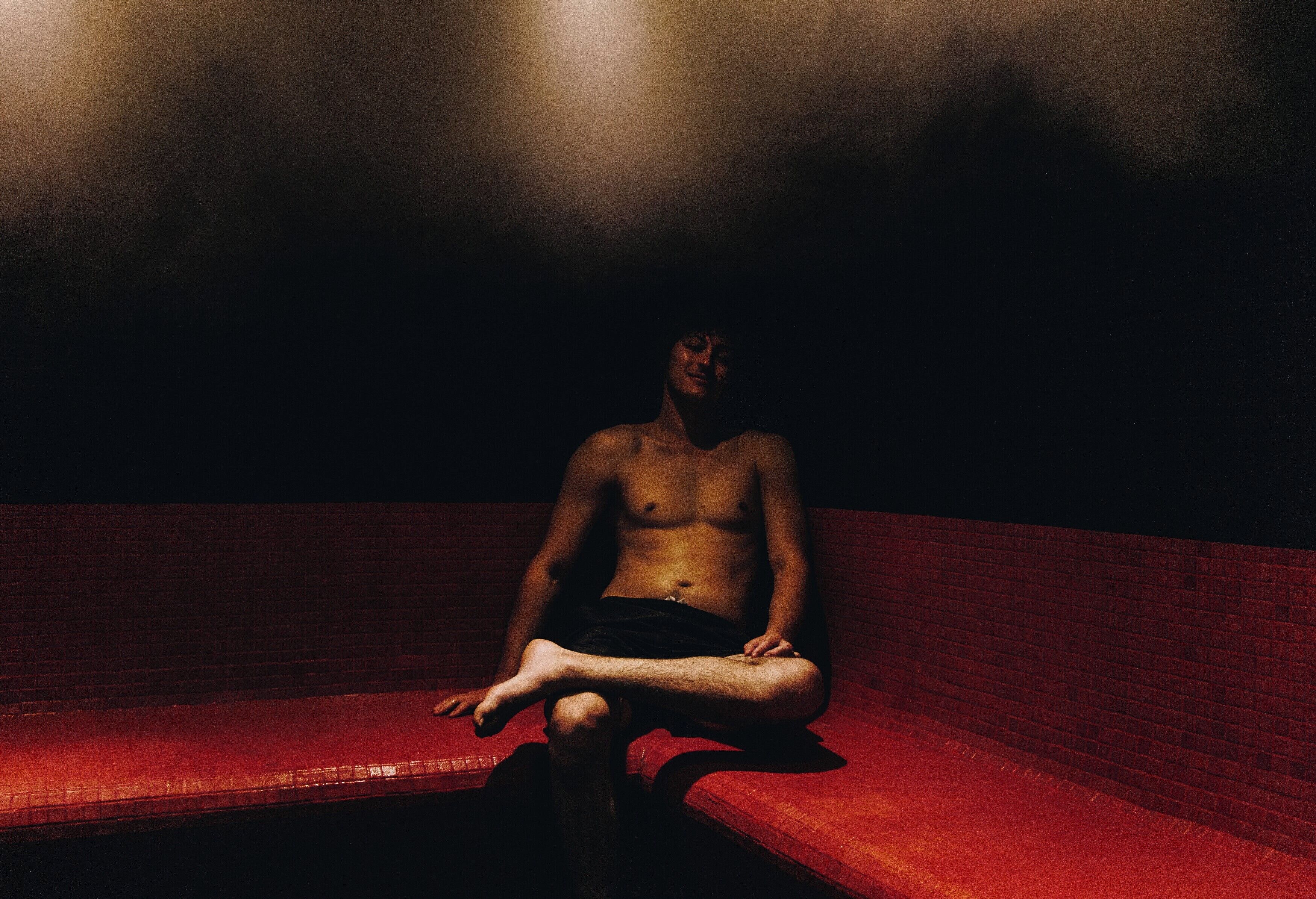 A person sitting on a bench in a dimly lit room with a red wall.