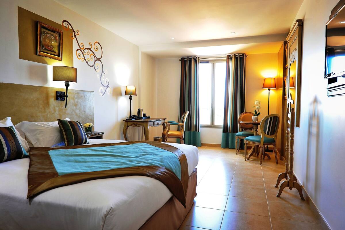 A hotel room with a bed, desk, chairs, and a TV.