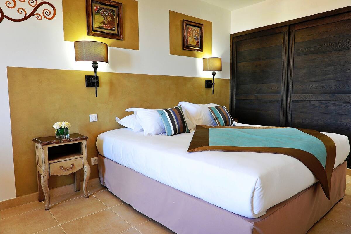 A bedroom with a bed, bedside lamps, a nightstand with a vase of flowers, and a large wardrobe.