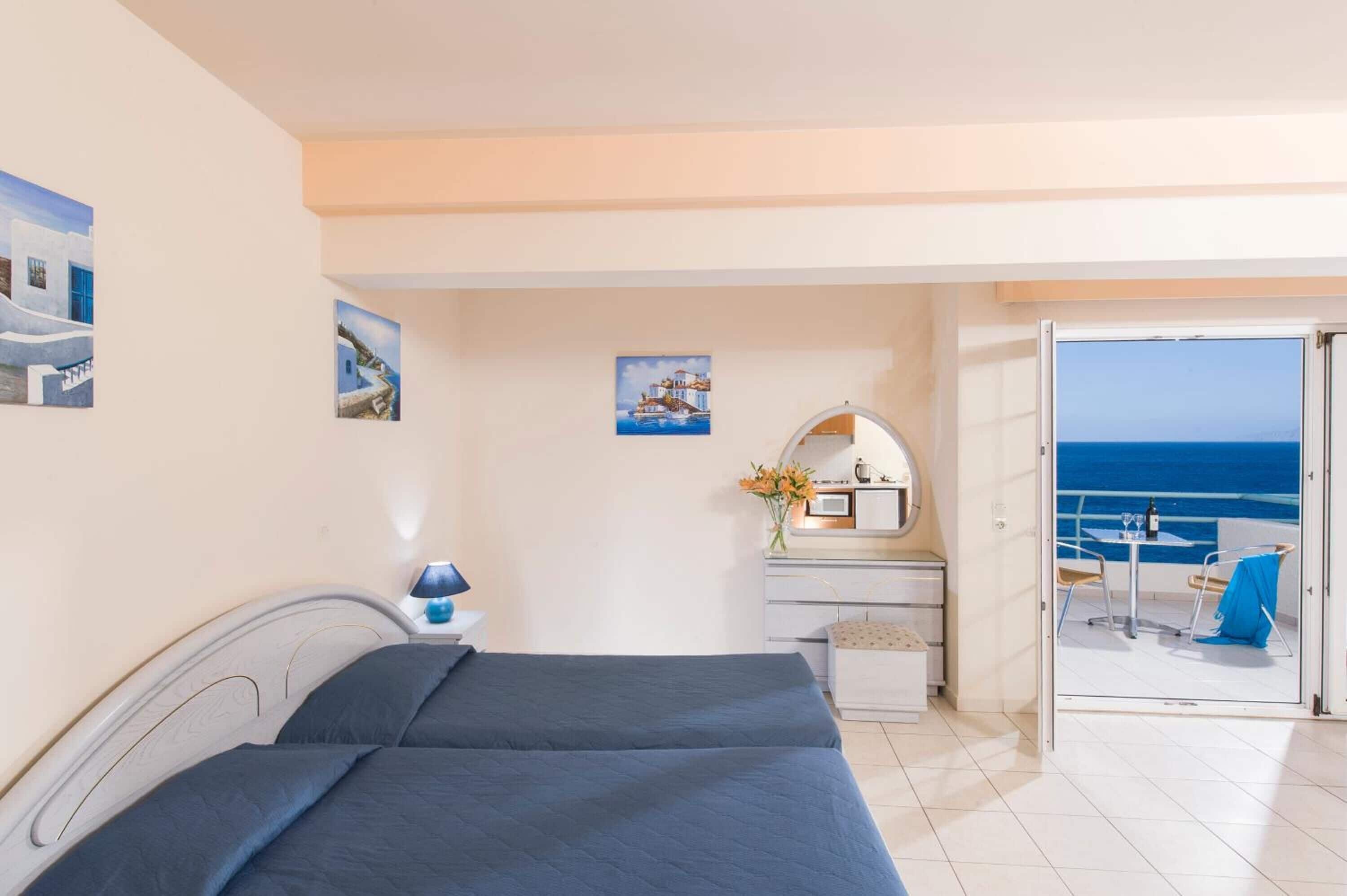 Une chambre à coucher avec un lit, un bureau doté d’un miroir et une vue sur la mer, visible à travers une porte ouverte.