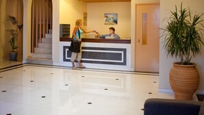 A hotel lobby with a reception desk, a staircase, and a large potted plant. - Creta Hotel (Agios Nikolaos)