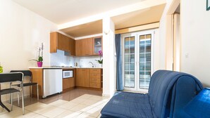 A compact living space with a kitchenette, a blue sofa, and a dining area. - Creta Hotel (Agios Nikolaos)