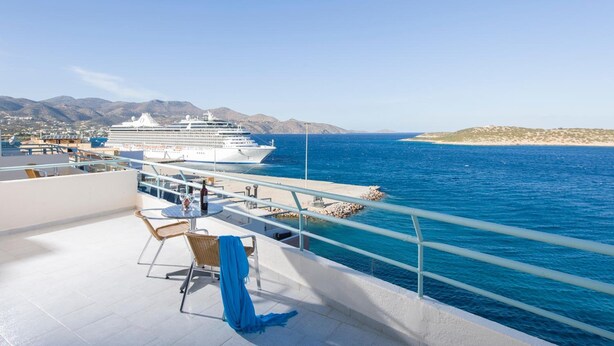 A cruise ship docked at a port with a clear blue sea and mountains in the background. - Creta Hotel (Agios Nikolaos)