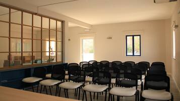 A conference room with a long table and rows of chairs, large windows, and a view of the outdoors.