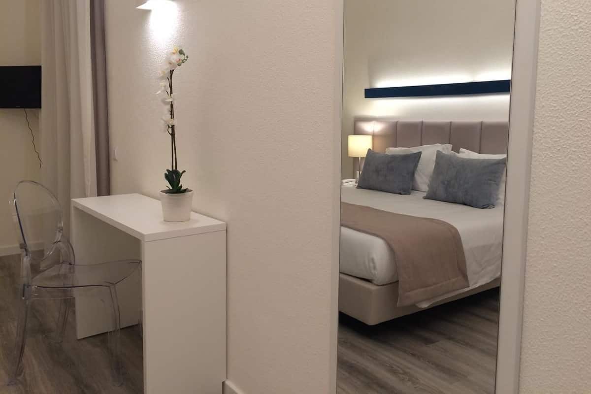 Een hotelkamer met een bed, nachtkastje en een spiegel die de kamer weerkaatst.