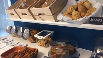 Buffet com diversos produtos de pastelaria, incluindo scones e doces, expostos em prateleiras.