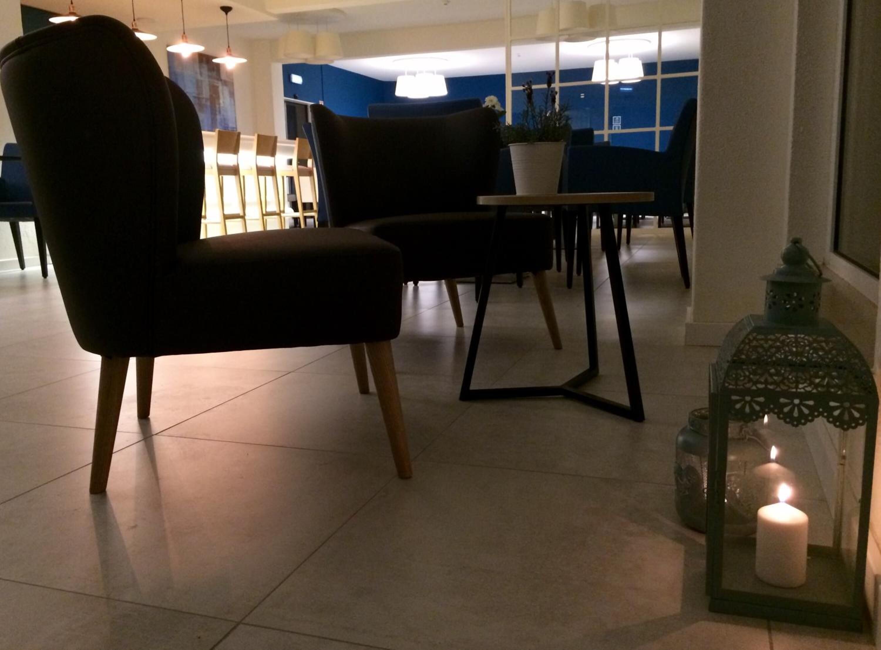 Um interior moderno com uma poltrona estofada escura, uma mesinha e uma vela acesa em um candeeiro.
