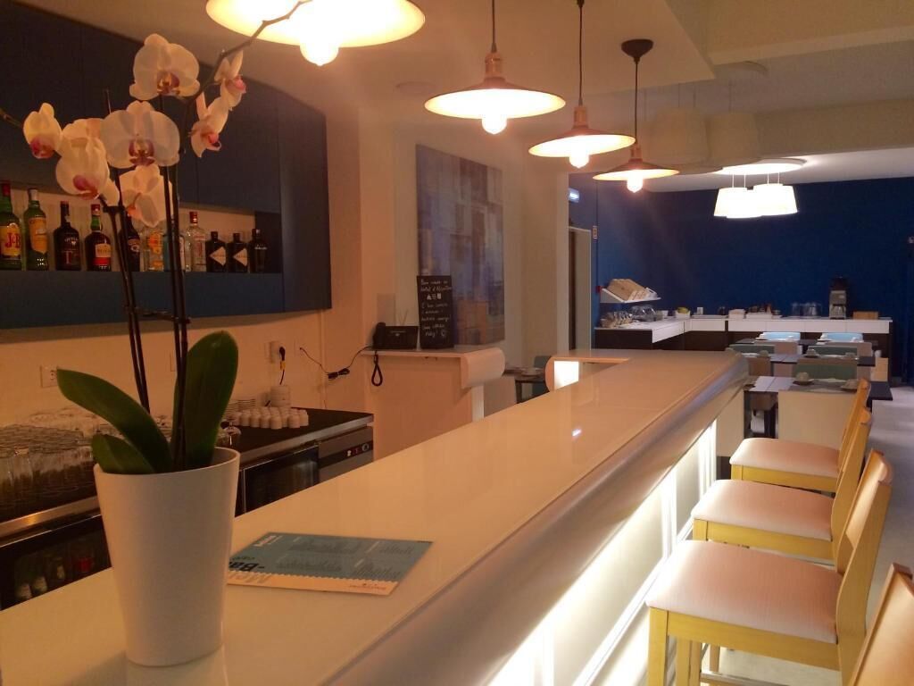 A bar area with a white counter, hanging pendant lights, and a potted orchid. There are chairs and a glimpse of a room with a blue wall and a poster.