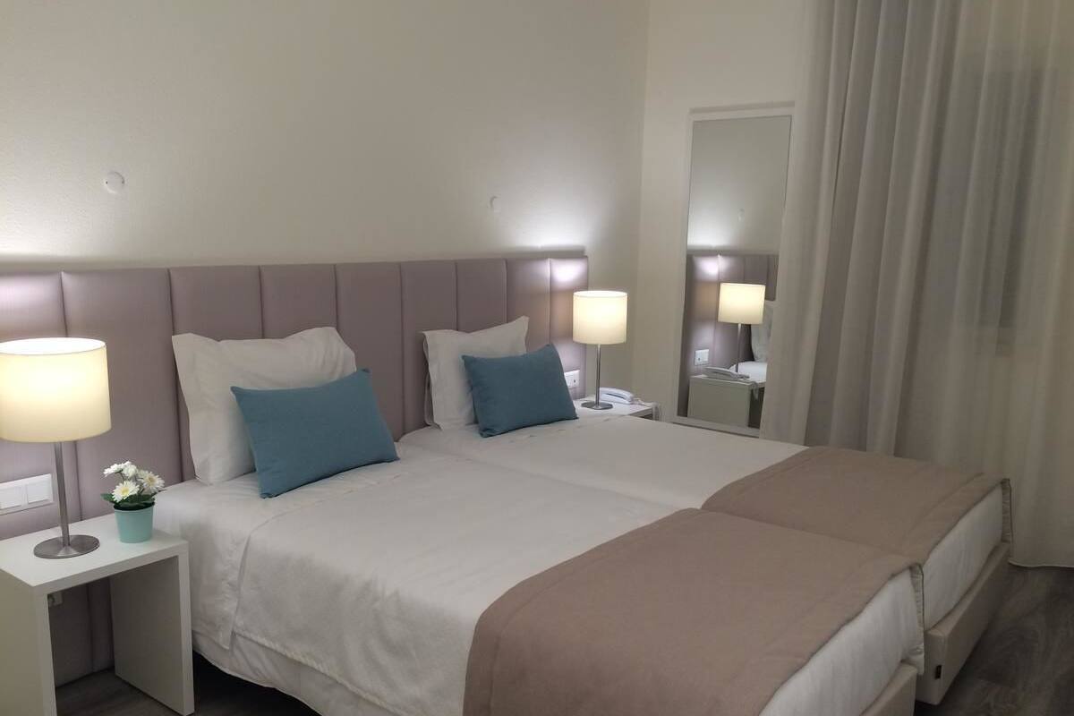 Een hotelkamer met twee bedden, een nachtkastje met een lamp en een spiegel.
