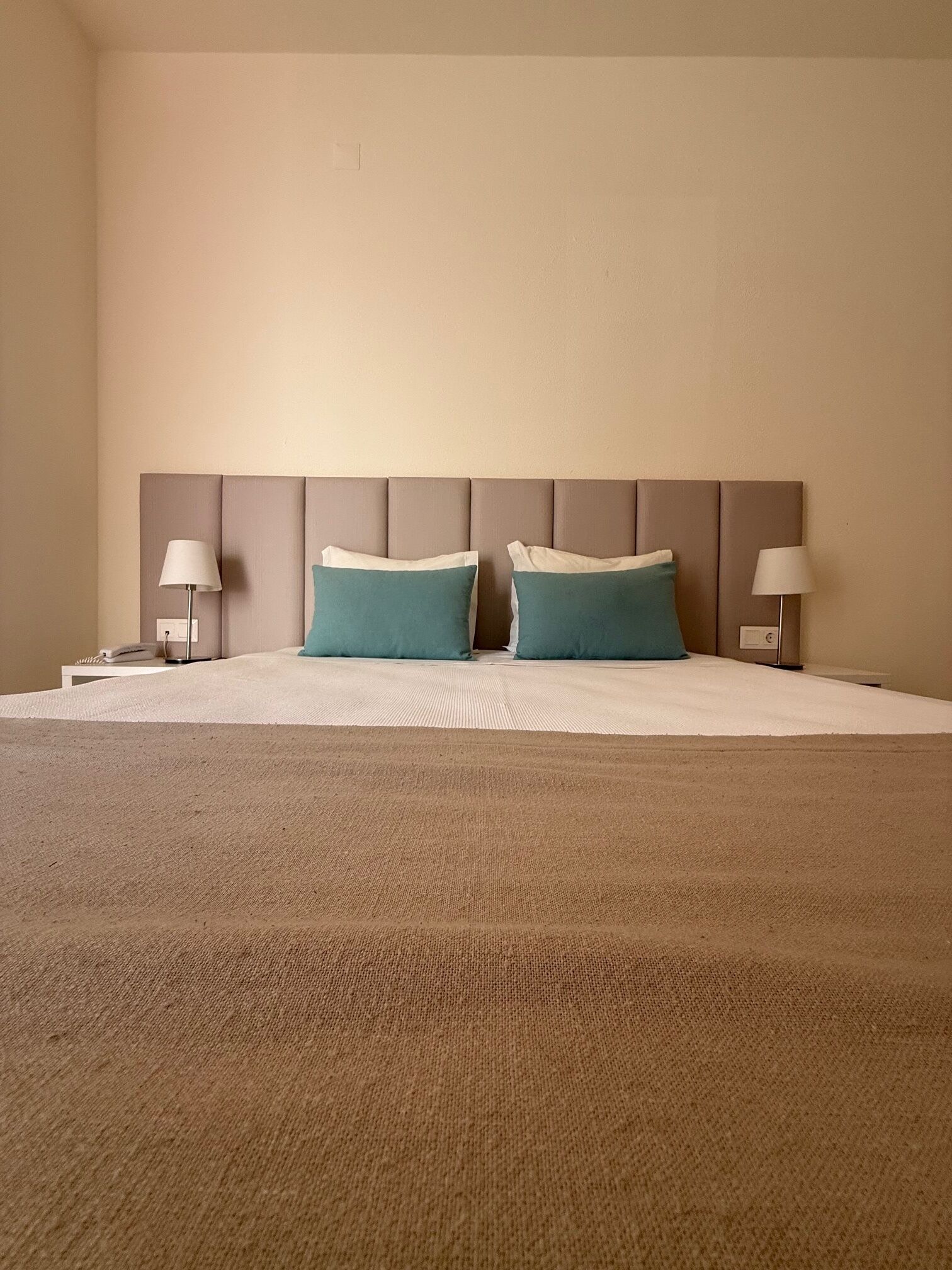 A hotel room with a large bed, two pillows, a headboard, bedside tables, and lamps.