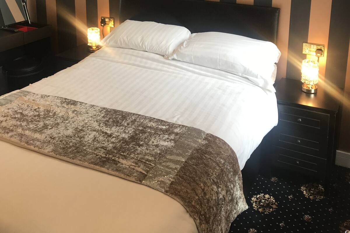Ein ordentlich bezogenes Bett mit weißen Leinen, ein dunkles Kopfteil und zwei Nachttischlampen.