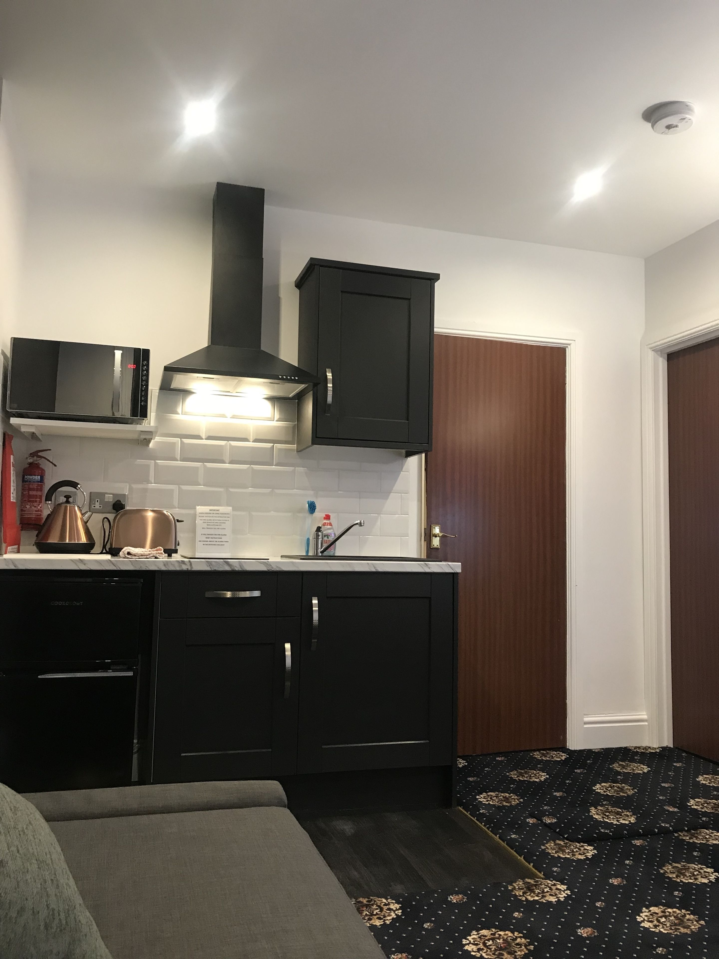 A compact kitchen with a microwave, kettle, toaster, and a stainless steel range hood.