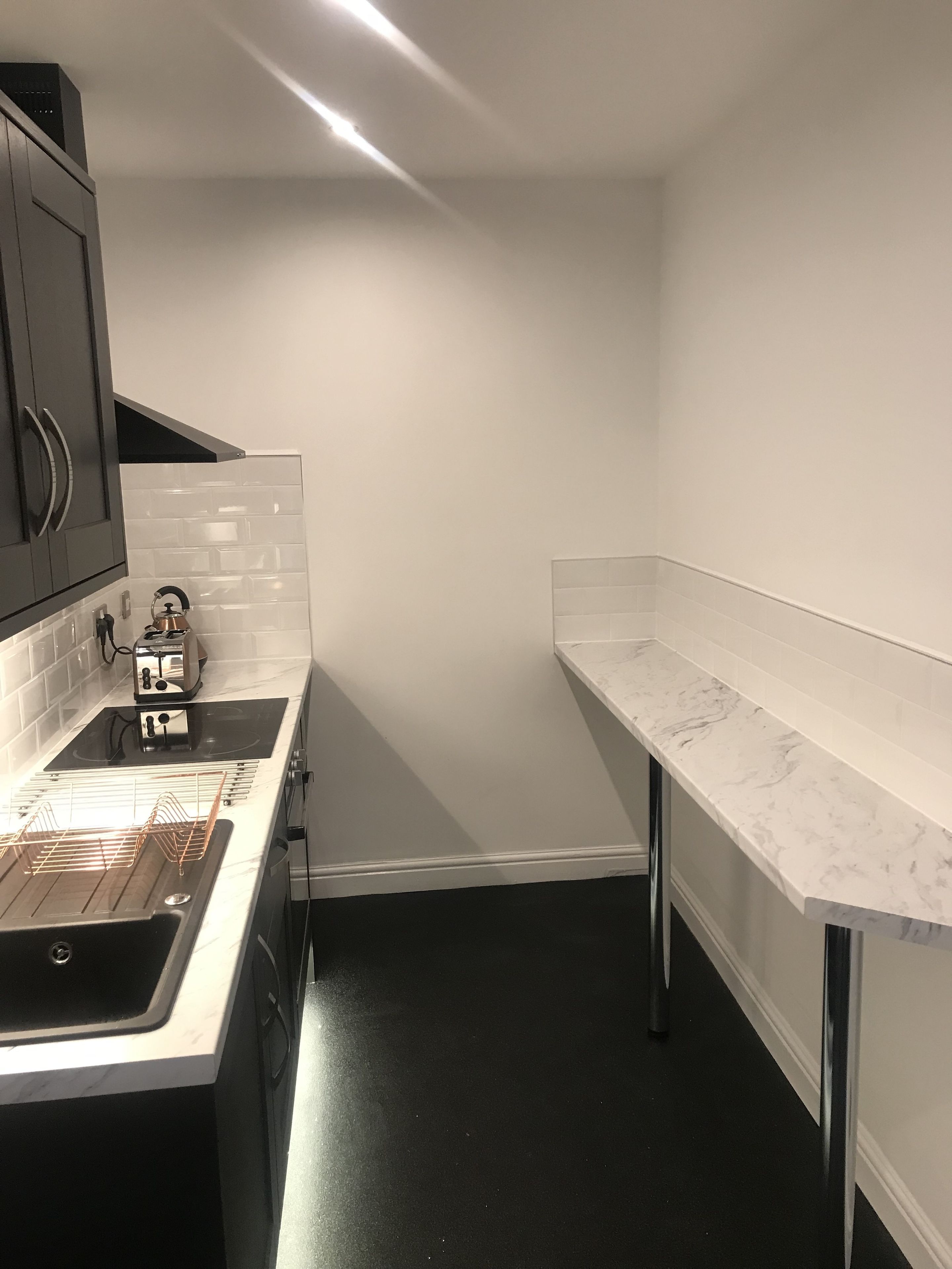 Et moderne køkken med sort bordplade, hvid bagplade og stålemmer.