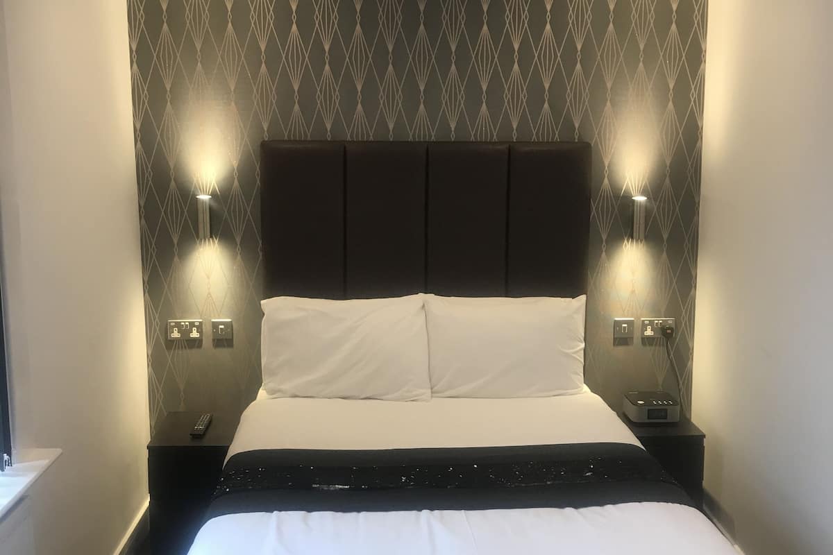 Ein Hotelzimmer mit einem großen Bett, zwei Nachttischen mit Lampen, einem Kopfteil mit geometrischem Muster und einer Bedieneinheit auf dem Seitentisch.