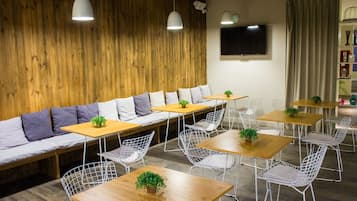 A modern cafe with wooden walls, white cushioned seating, and metal wire chairs.