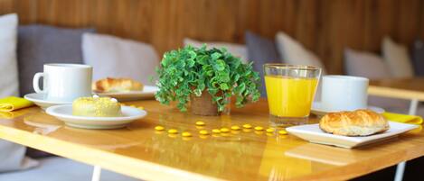 A breakfast table with a white mug, a glass of orange juice, a small plant, and pastries.