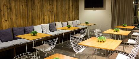 A modern cafe with wooden walls, a sofa with cushions, and tables with chairs.
