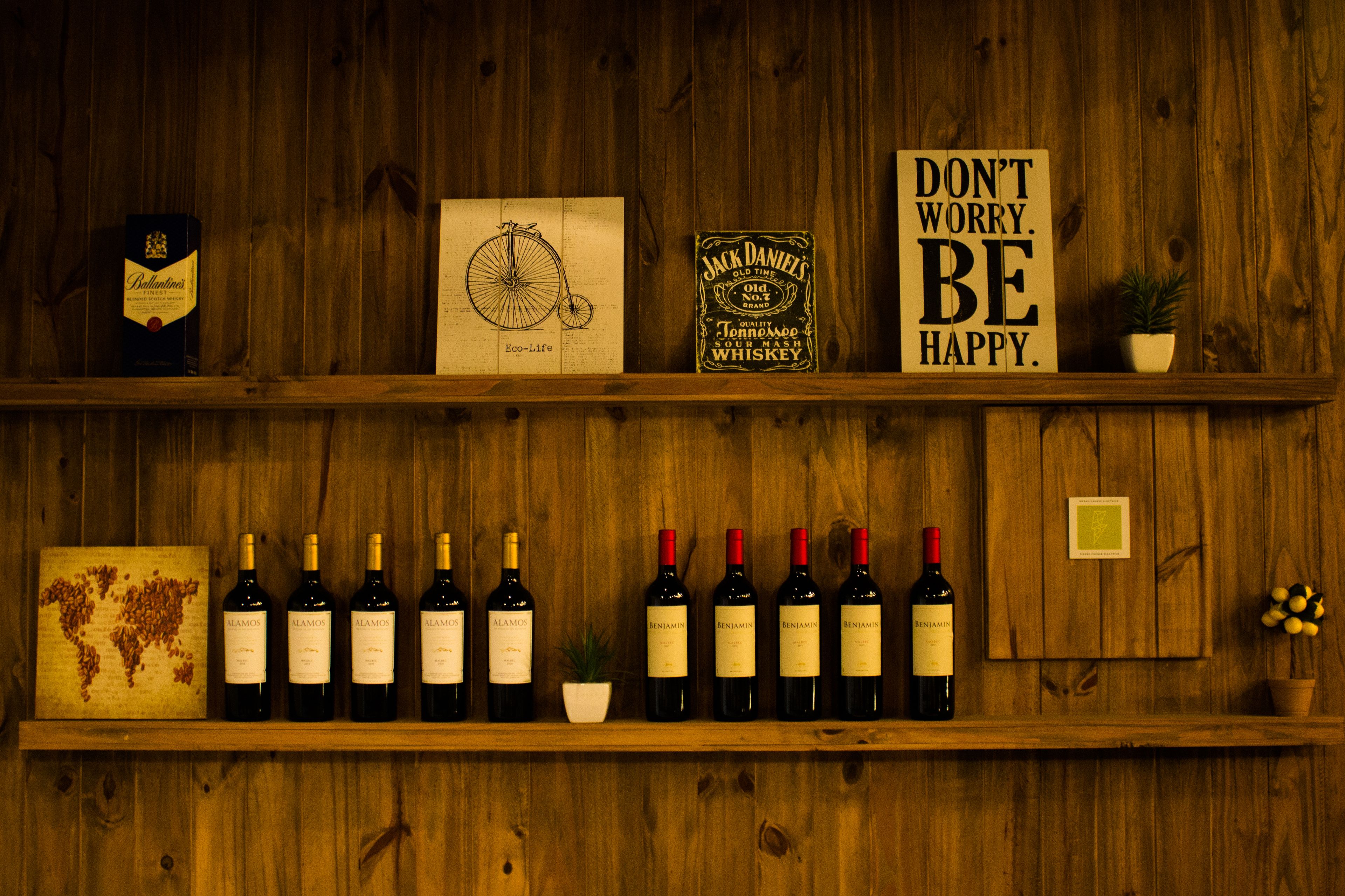 Eine Holzwand mit Regalen, auf denen Weinflaschen, eine Weltkarte und ein Schild mit der Aufschrift 'DON'T WORRY. BE HAPPY' ausgestellt sind.