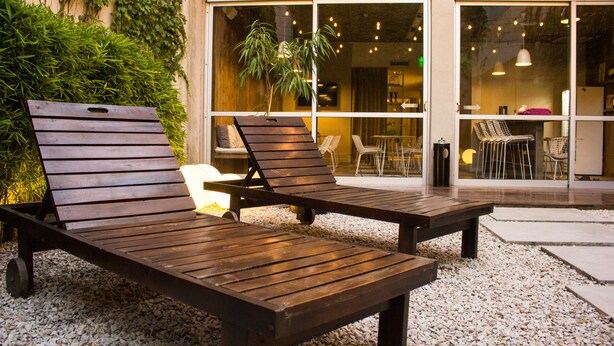 Two wooden lounge chairs in front of a building with a glass door, a potted plant, and a sign indicating an exit.