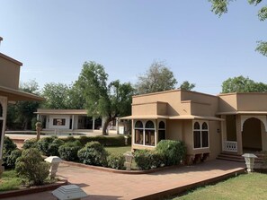 A courtyard with a building featuring arched windows and a covered walkway. - Heritage Resort (Bikaner)