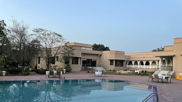 Una piscina con indicador de profundidad, mobiliario exterior y un edificio con terraza cubierta.