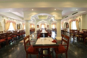 A spacious dining hall with multiple tables and chairs, high ceilings, and decorative arches. - Heritage Resort (Bikaner)