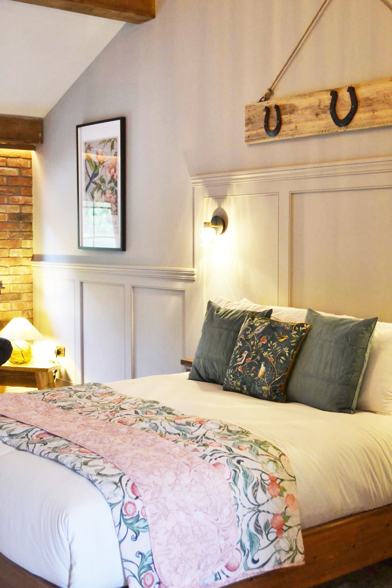 A neatly made bed with floral bedding, a wall-mounted light fixture, and a rustic wooden sign with horseshoes.