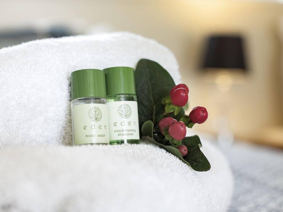 Duas embalagens de gel de banho Eden e shampoo condicionador sobre uma toalha branca com bagas vermelhas.