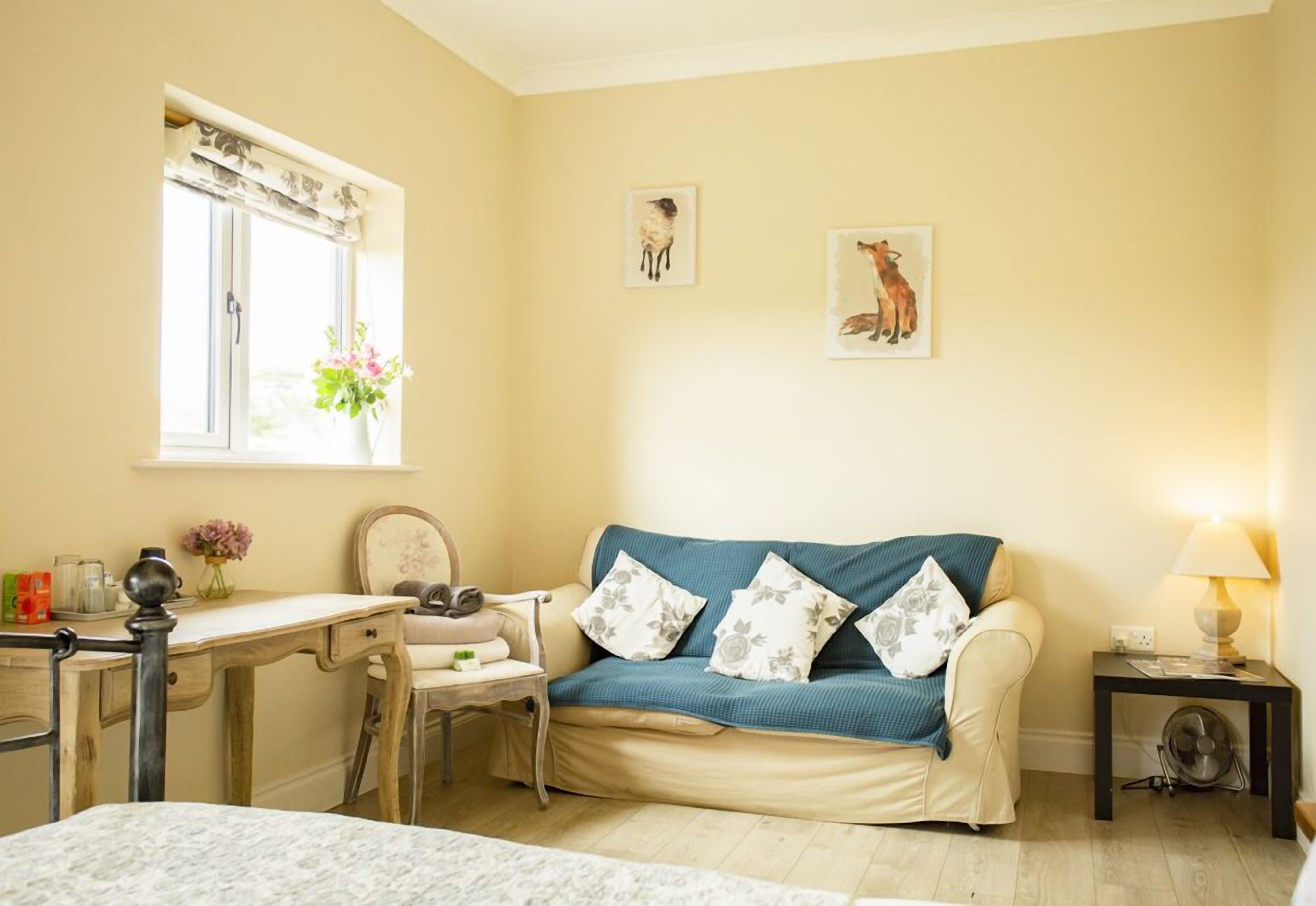 A cozy room with a sofa, a desk, and a chair. There are two framed pictures on the wall.