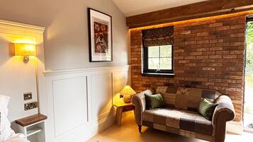 Ein gemütliches Zimmer mit Backsteinwand, Holzboden und einer Decke, einer Couch, einer Lampe und einem gerahmten Bild an der Wand.