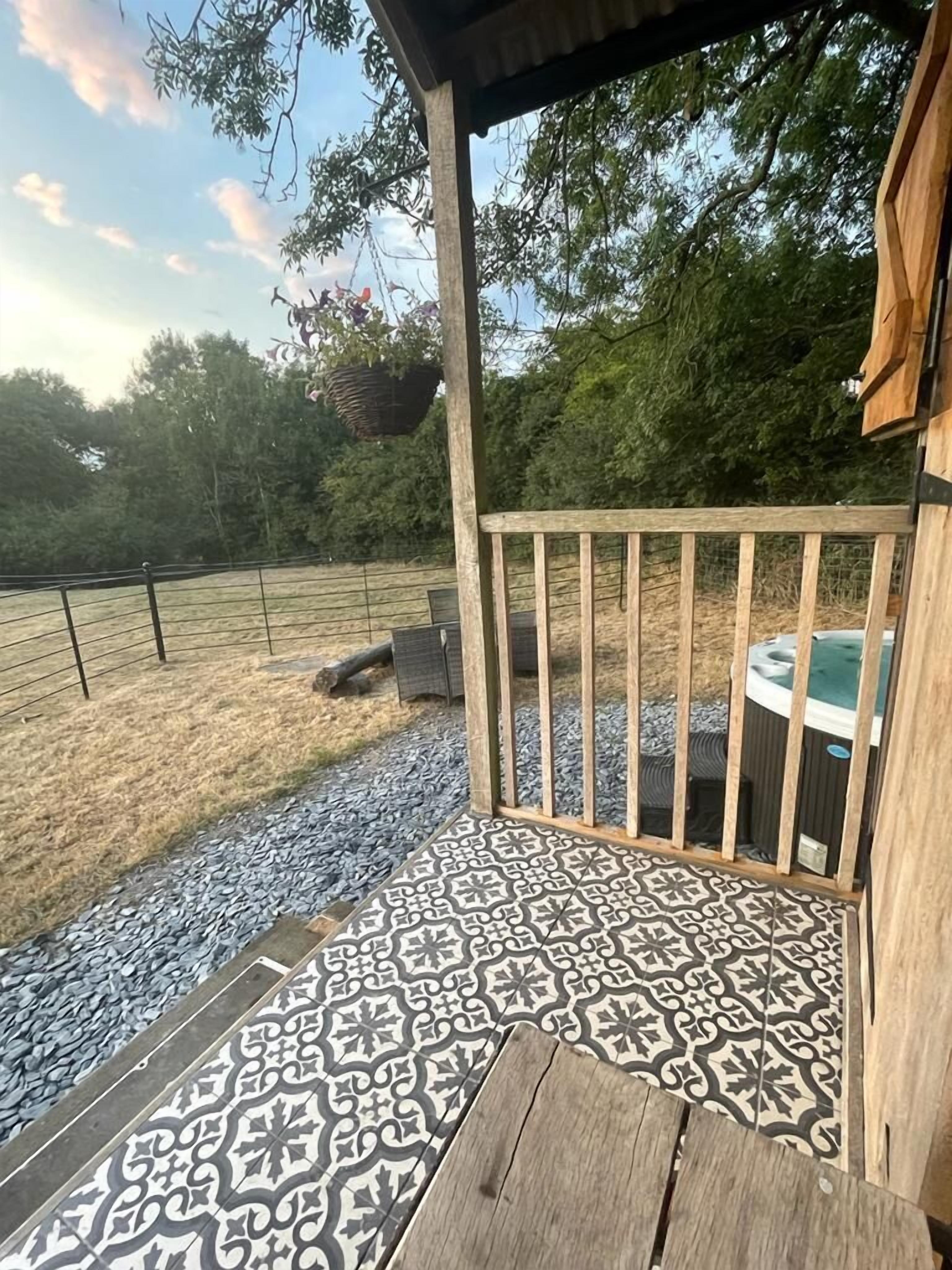 Un patio techado con piso de baldosas estampadas, baranda de madera y un jacuzzi al fondo.