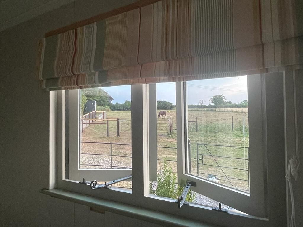 Ein Fenster mit Blick auf eine eingezäunte Außenanlage, eine Metallleiter und eine Holzkonstruktion im Hintergrund.