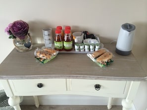 A wooden table with a vase of purple flowers, two sandwiches, several bottles of drinks, and a coffee maker. - Hillcroft Accommodation (Bristol)