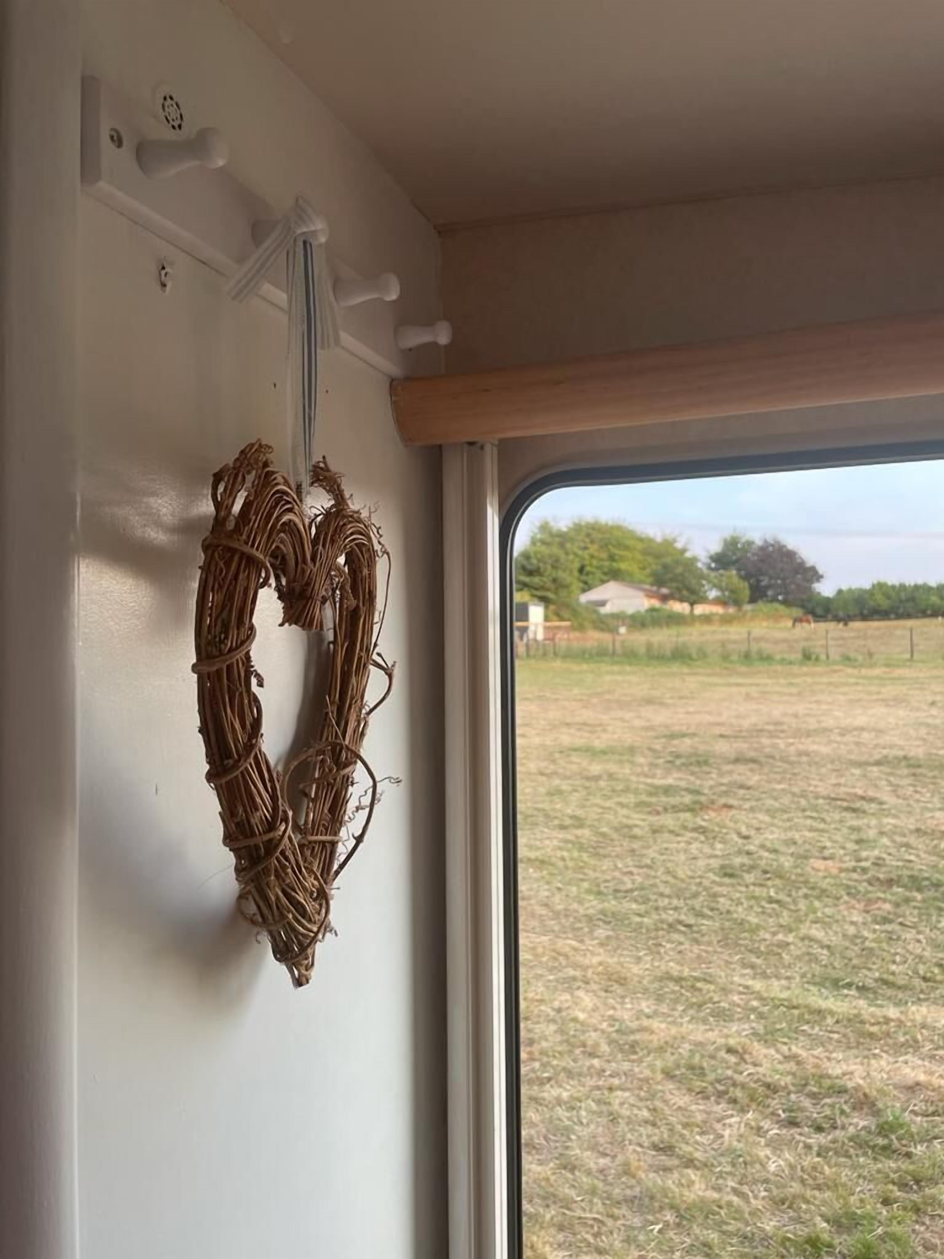 Una ventana con un adorno en la pared interior, vista de un campo cubierto de hierba y árboles al exterior.