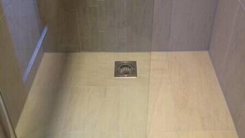 A small, enclosed shower area with tiled walls and floor, featuring a drain in the center.