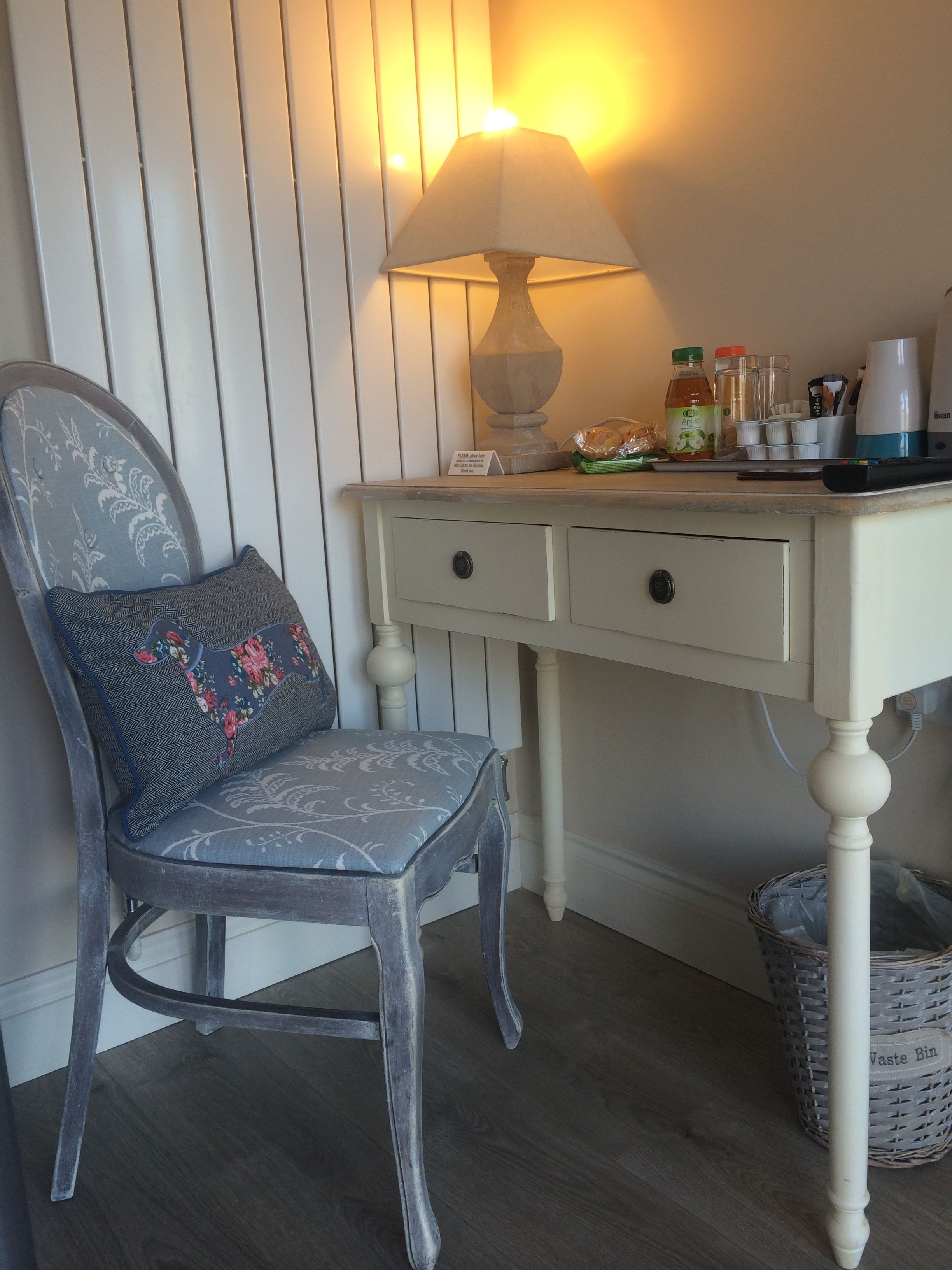 A chair with a floral cushion, a table with a lamp, and a basket labeled "Waste Bin".